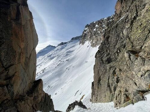 Vue depuis un couloir enneigé encadré par des parois rocheuses, révélant les flancs enneigés de la montagne dans le cœur du Parc Naturel de Posets-Maladeta en Espagne, découvert lors d'un raid à ski visant l'ascension de l'Aneto, le plus haut sommet des Pyrénées, encadré par un guide de haute montagne de Sensations Pyrénées.