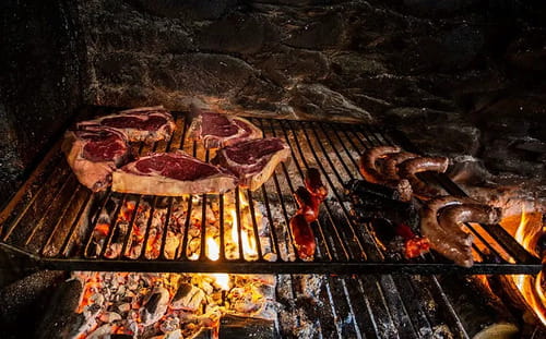 Grillades d'entrecôtes et saucisses sur le feu de cheminée dans le restaurant du refuge de Montgarri, Val d'Aran, Espagne, lors d'une pause culinaire pendant un raid à ski.