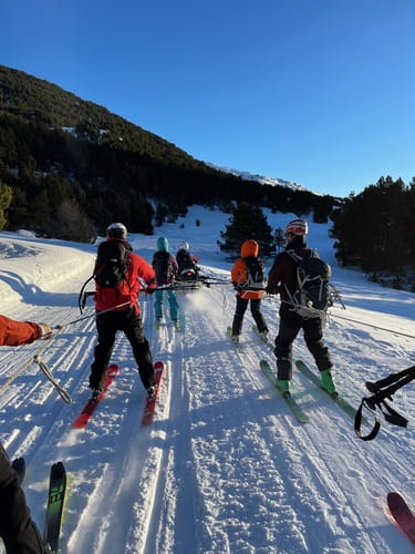 Skieurs de randonnée tractés par une motoneige lors d'un raid à ski partant de Baqueira jusqu'à Montgarri, dans un décor hivernal de sapins enneigés.