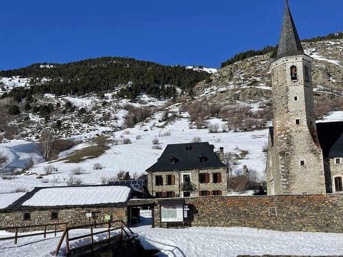 Extérieur du Refuge de Montgarri, situé dans un cadre historique et pittoresque du Val d'Aran, Catalogne, Espagne, accessible par un pont, dans un environnement enneigé sous un ciel bleu, idéal pour les raids à ski de randonnée encadrés par un guide de haute montagne de Sensations Pyrénées.