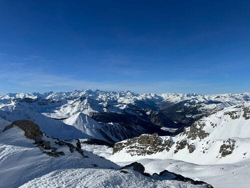 Vue panoramique depuis un sommet offrant une perspective sur de nombreux autres sommets dans le Parc Naturel du Queyras, sous un ciel bleu éclatant, lors d'un raid à ski encadré par un guide de haute montagne de Sensations Pyrénées