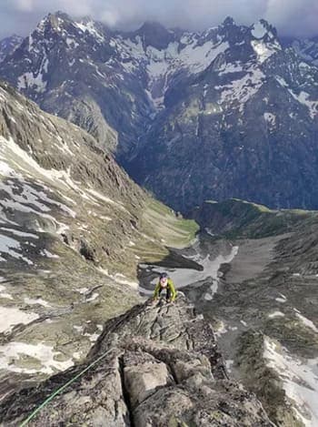 Paysage de haute montagne avec des sommets parsemés de plaques de neige printanière, un alpiniste escaladant la roche pour atteindre le sommet.