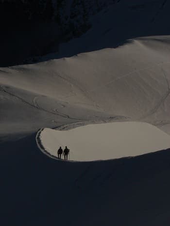 Deux alpiniste redescendant de leur sommet à l'ombre  dans un décors immaculé de neige.