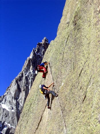 Deux grimpeurs escaladant activement une paroi rocheuse verticale en utilisant une fissure comme prise principale.
