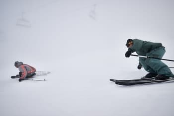 Deux skieurs en descente hors-piste, alignant les virages dans un paysage brouillé et immaculé de neige, avec un environnement entièrement blanc autour d'eux