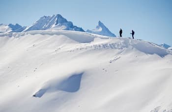 Deux freerideurs sur le point de débuter une descente raide, seuls au monde, dans un vaste paysage enneigé.