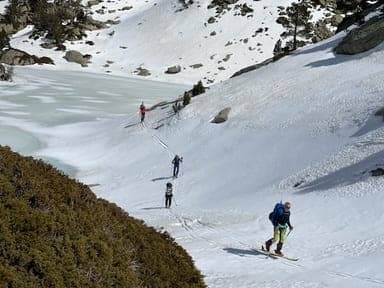 Groupe de skieurs de randonnée dans les Encantats, rejoignant le prochain refuge de leur raid à ski, longeant un lac encore partiellement glacé au début du printemps.