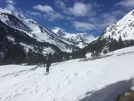 Skieur de randonnée progressant dans la vallée du Galbe sur un terrain plat enneigé, entouré d'un décor de sapins mêlés à la neige.